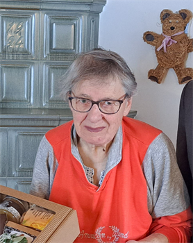 Eine ältere Frau mit Brille und rotem Hemd sitzt vor einem Stofftier